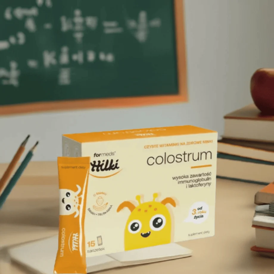 HILKI COLOSTRUM - bezpieczny suplement z colostrum dla najmłodszych opakowanie na tle tablicy szkolnej