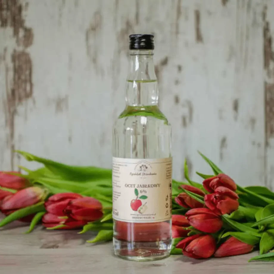 Butelka octu jabłkowego ogródek dziadunia na tle czerwonych tulipanów.