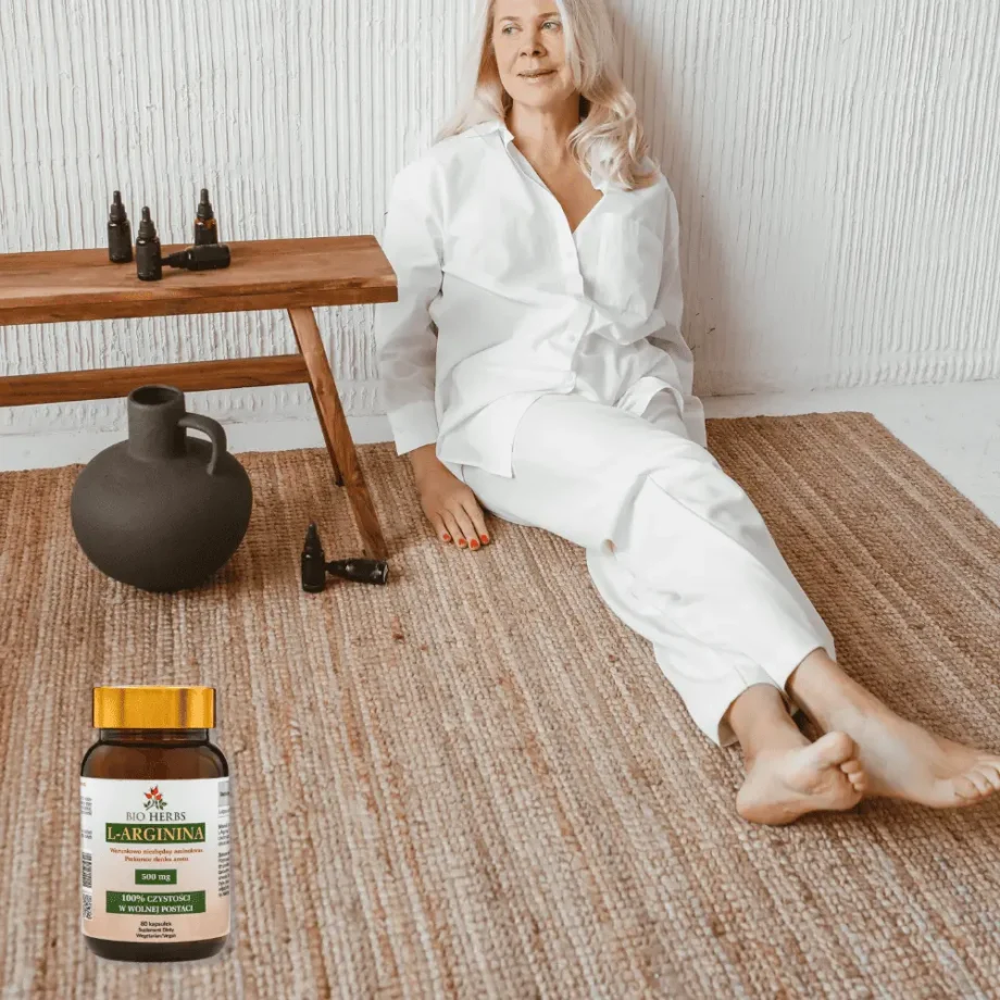 Siedząca, dojrzała kobieta na podłodze, w tle słoik z suplementem diety l-arginina bio herbs